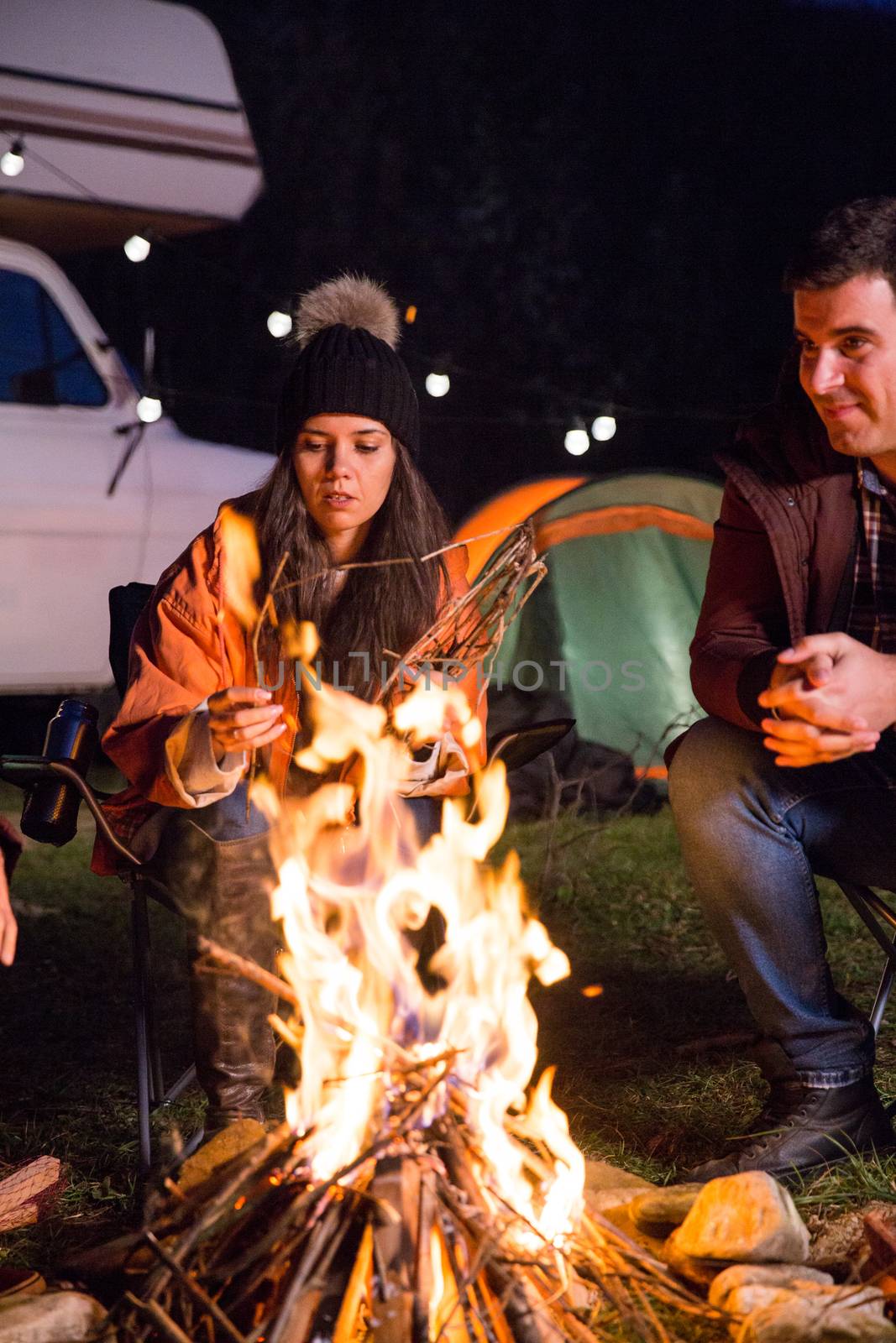 Girl with her friends relaxing together in camp site around camp fire in the mountains. Retro camper van.