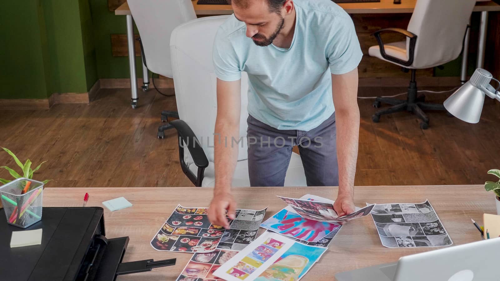 Young designer who looks over some printed pictures. New project and modern office