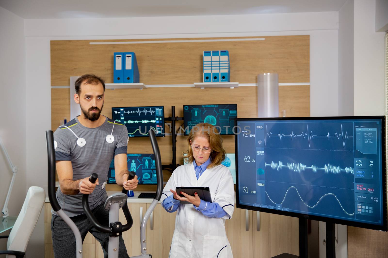 Male athlete who makes a physical effort on the stepper and has electrodes attached to him and the doctor who follows the evolution of his tablet. Modern sports laboratory