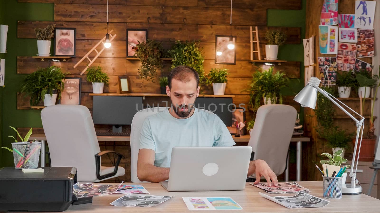 Young designer working on a laptop surrounded by print photographers. Caucasian professional artist