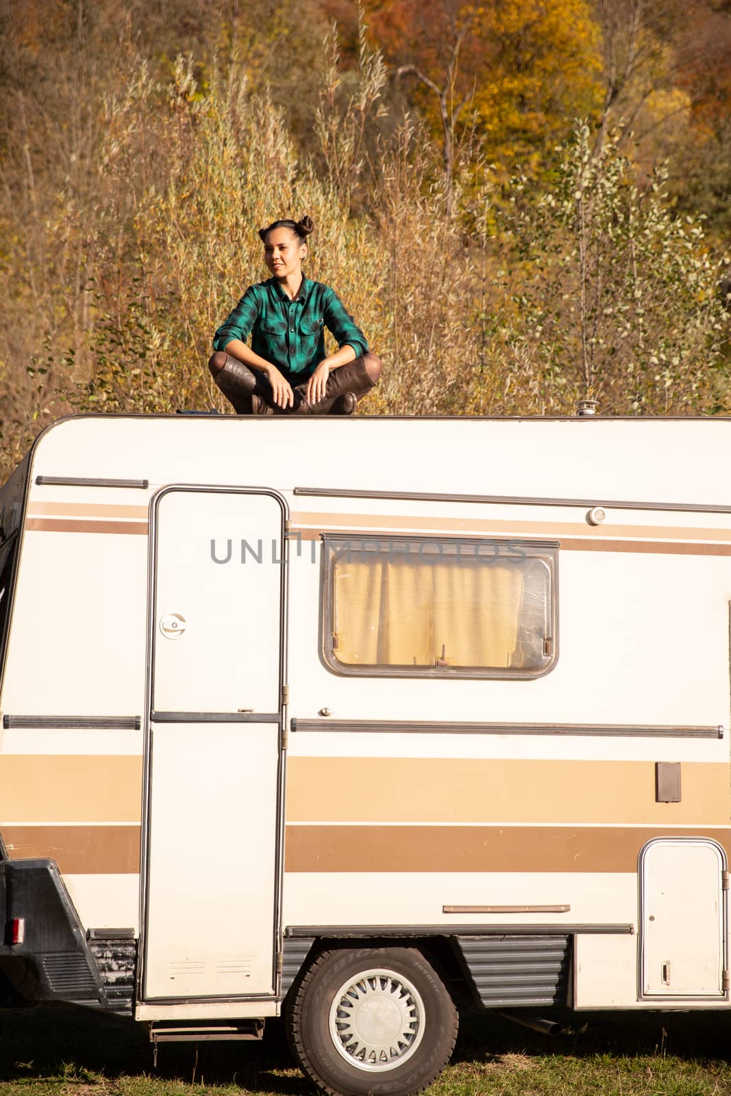 Young girl sitting on the roof of a retro camper and admiring the autumn view. Relaxing vacation