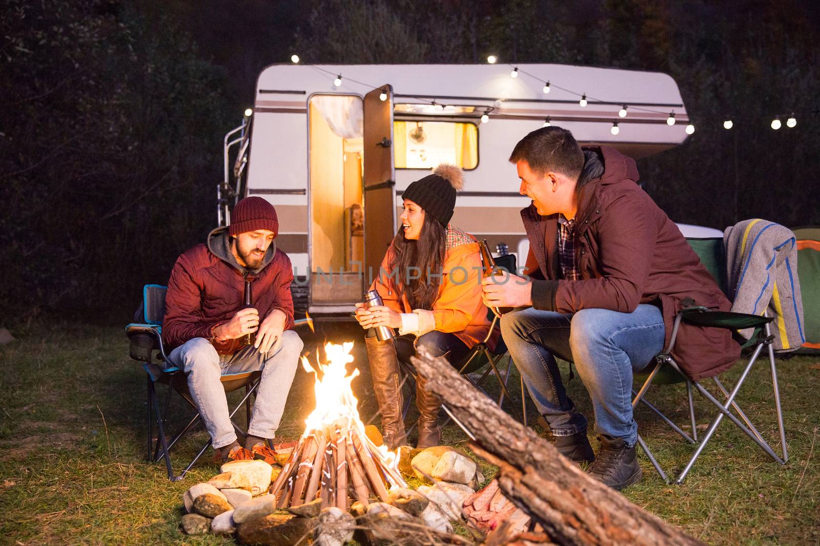 Group of close friends camping together in the mountains relaxing around camping fire. Retro camper van. Nature clean air.