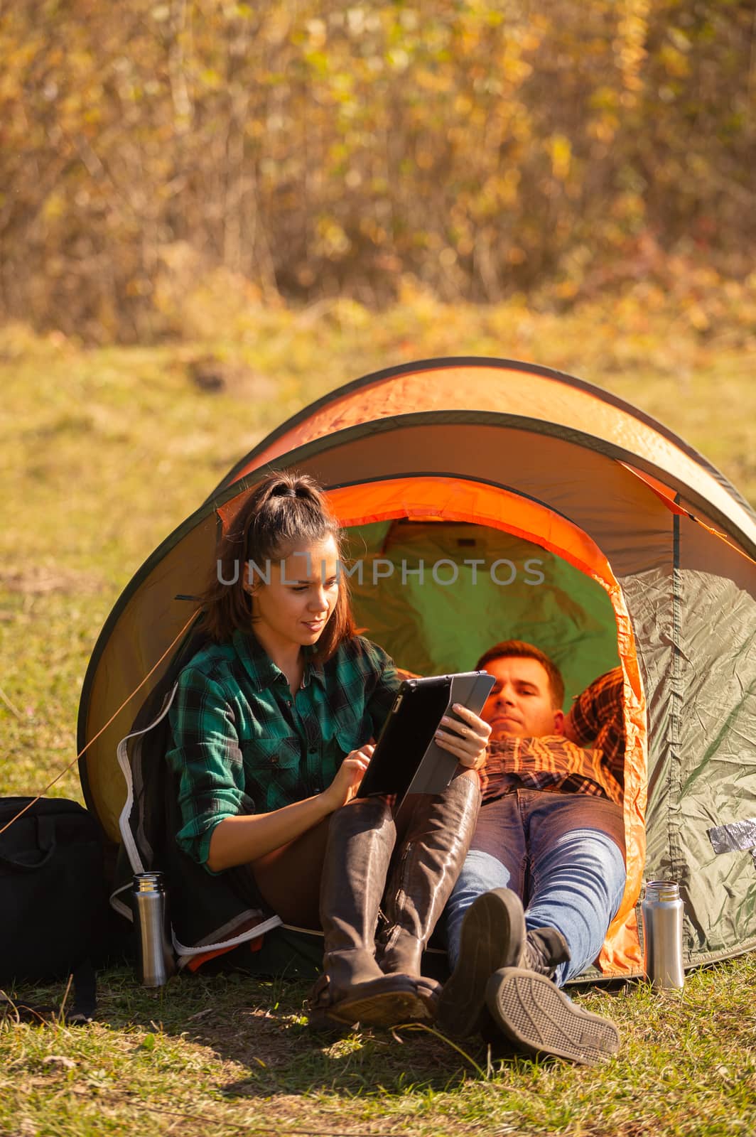 Young girl working on the tablet her friend next to the tent. Outdoor activity