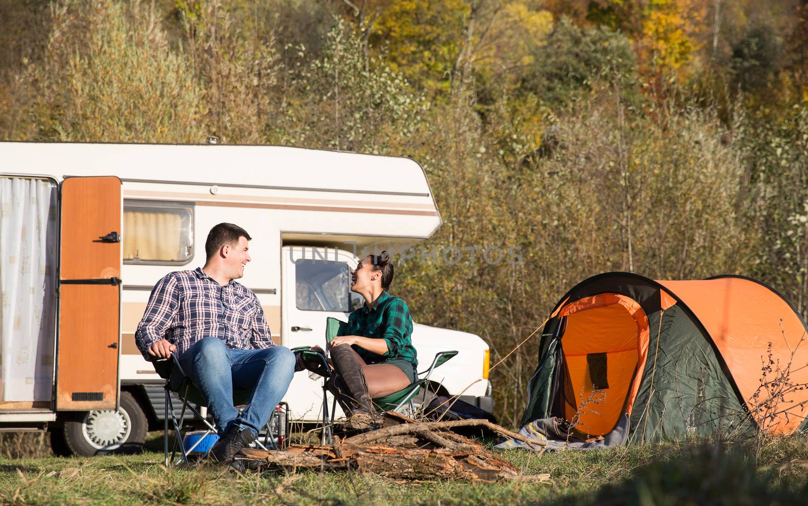 Happy couple in autumn relaxing tegether in a campsite. Retro camper van.