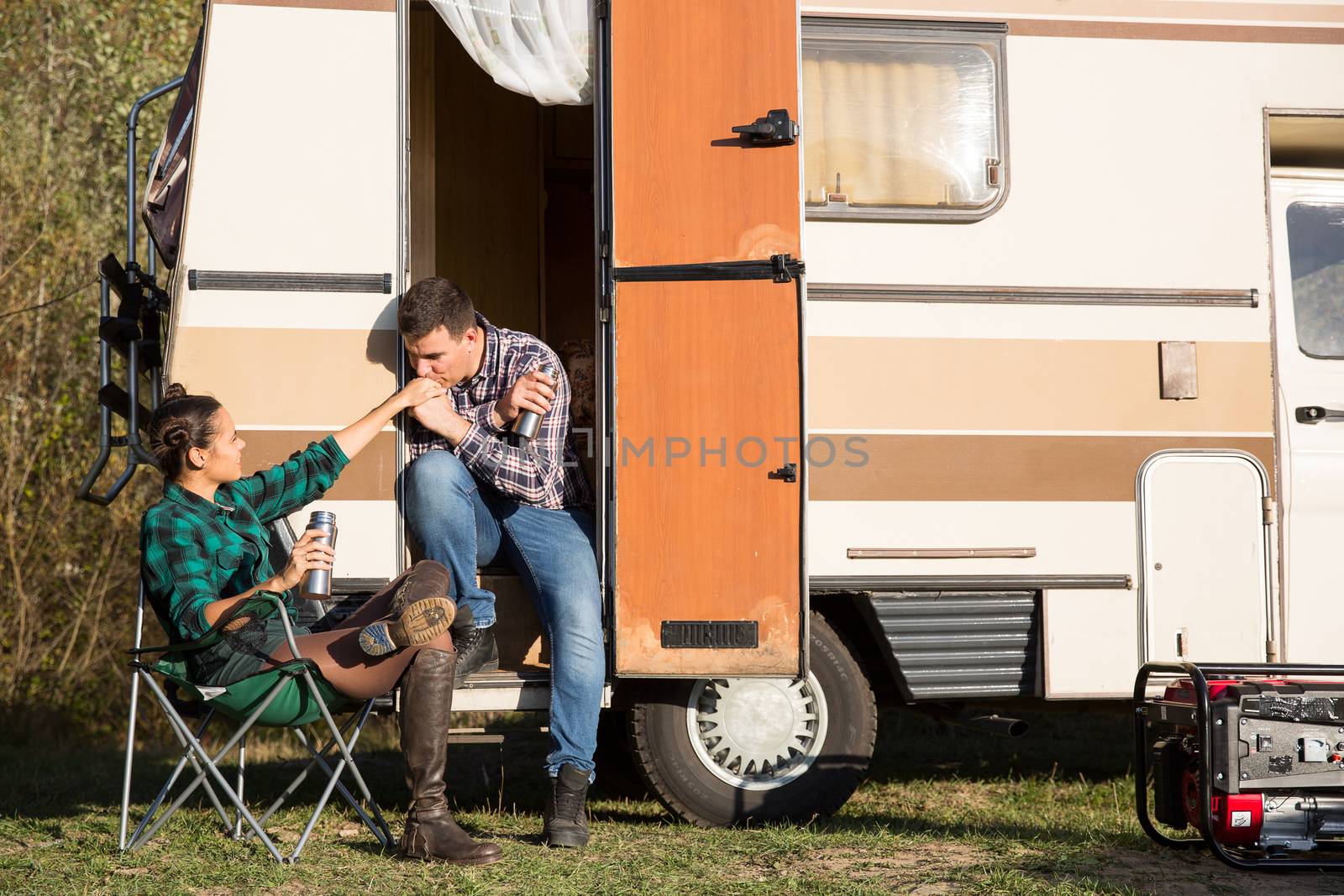 Man showing his love for his girlfriend in front of their retro camper van by kissing her hand.