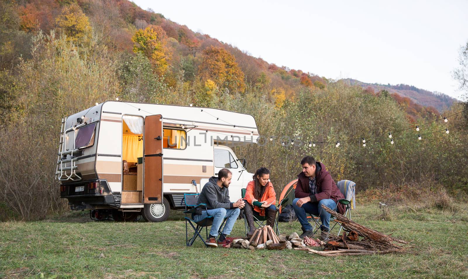 Group of friends enjoying their time together in the mountains. Friends camping and retro camper van in the background.