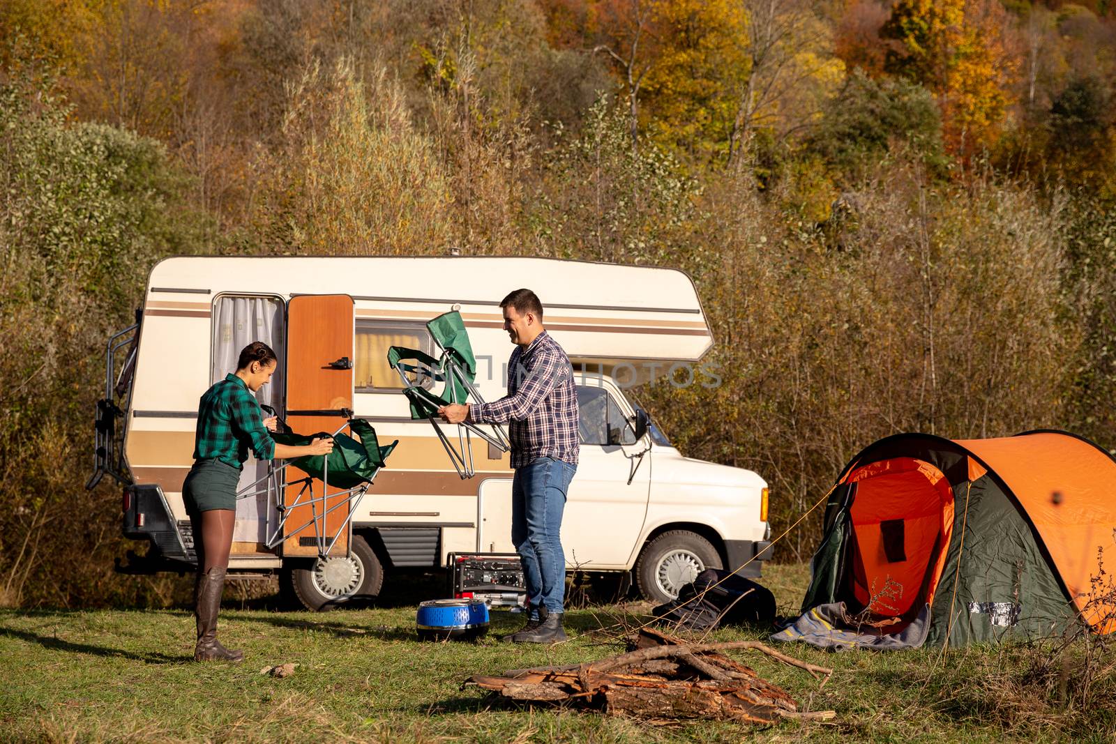 Couple of lovers who install their camping chairs in campsite. Retro camper in the background