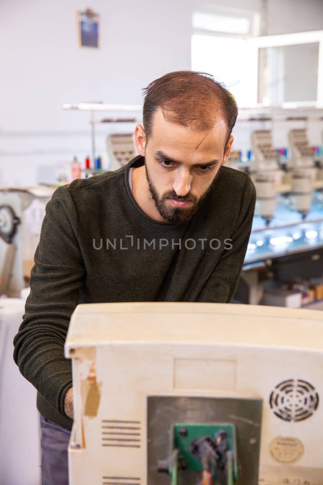 Young worker from the textile factory who controls an embroidery machine. Textile industry