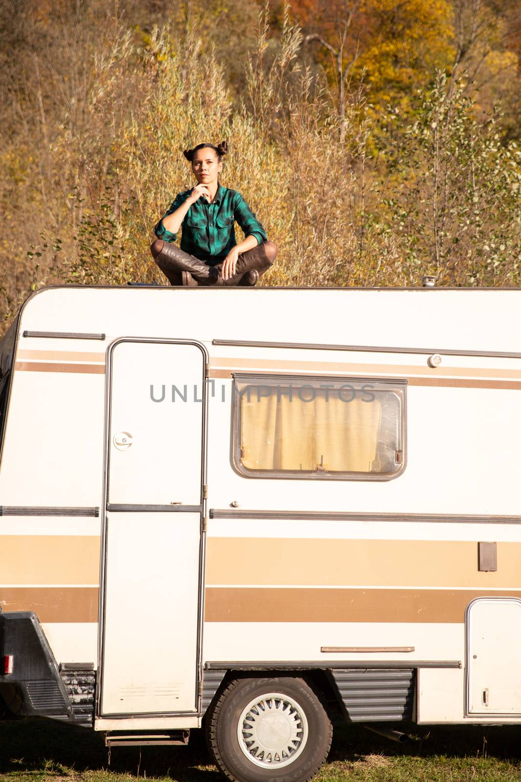 Pensively girl sits on the roof of a retro camper. Mountain adventure