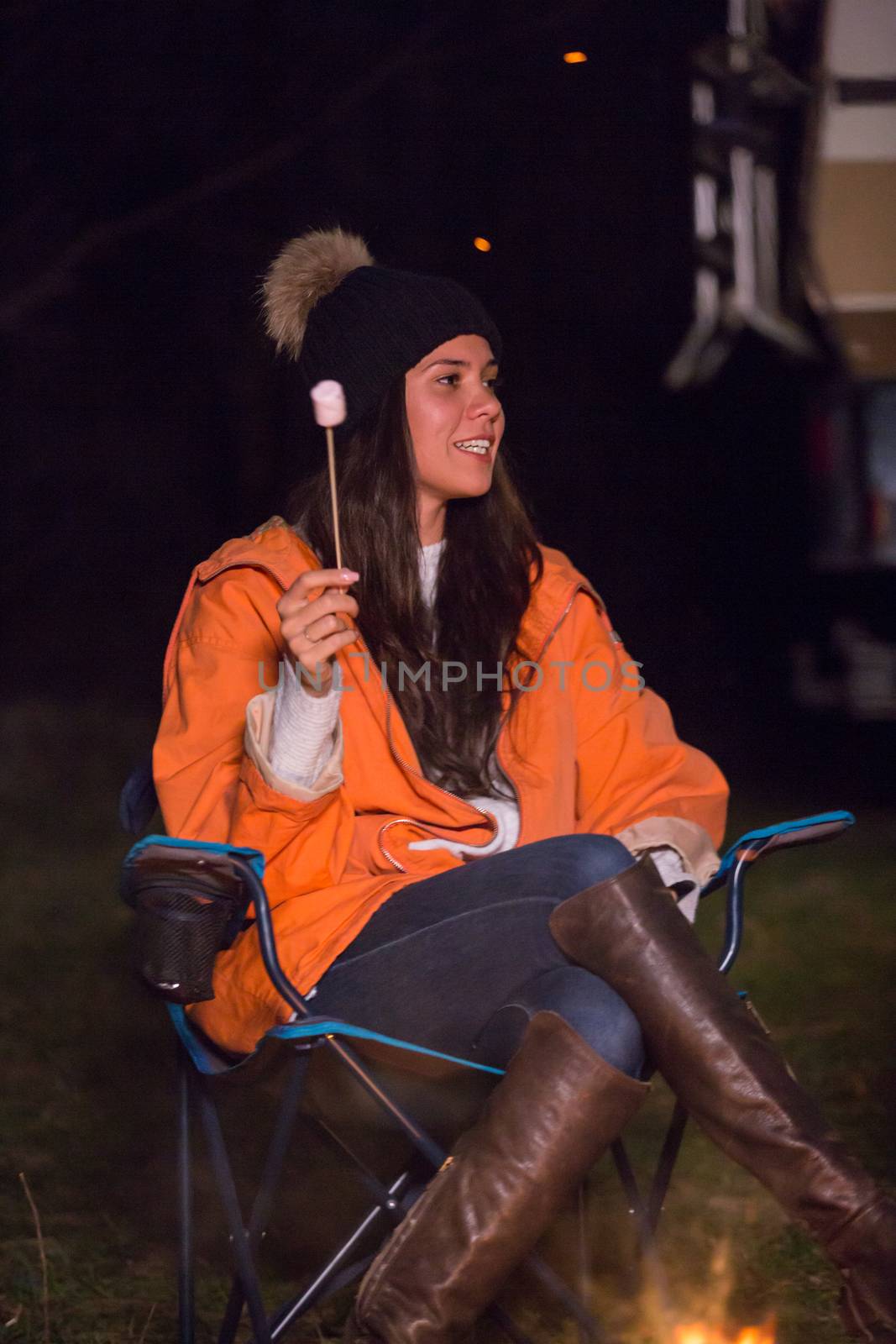 Funny young girl holding a stick with marshmallow around camp fire. Smiling girl in campsite.