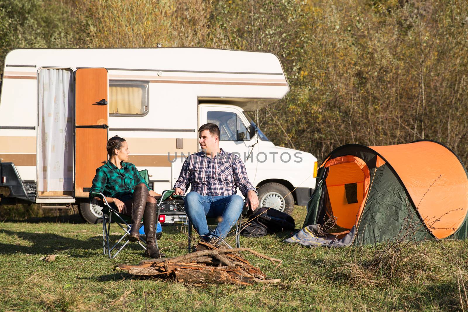 Beautiful young couple relaxing together in the mountains with their retro camper van in the background.