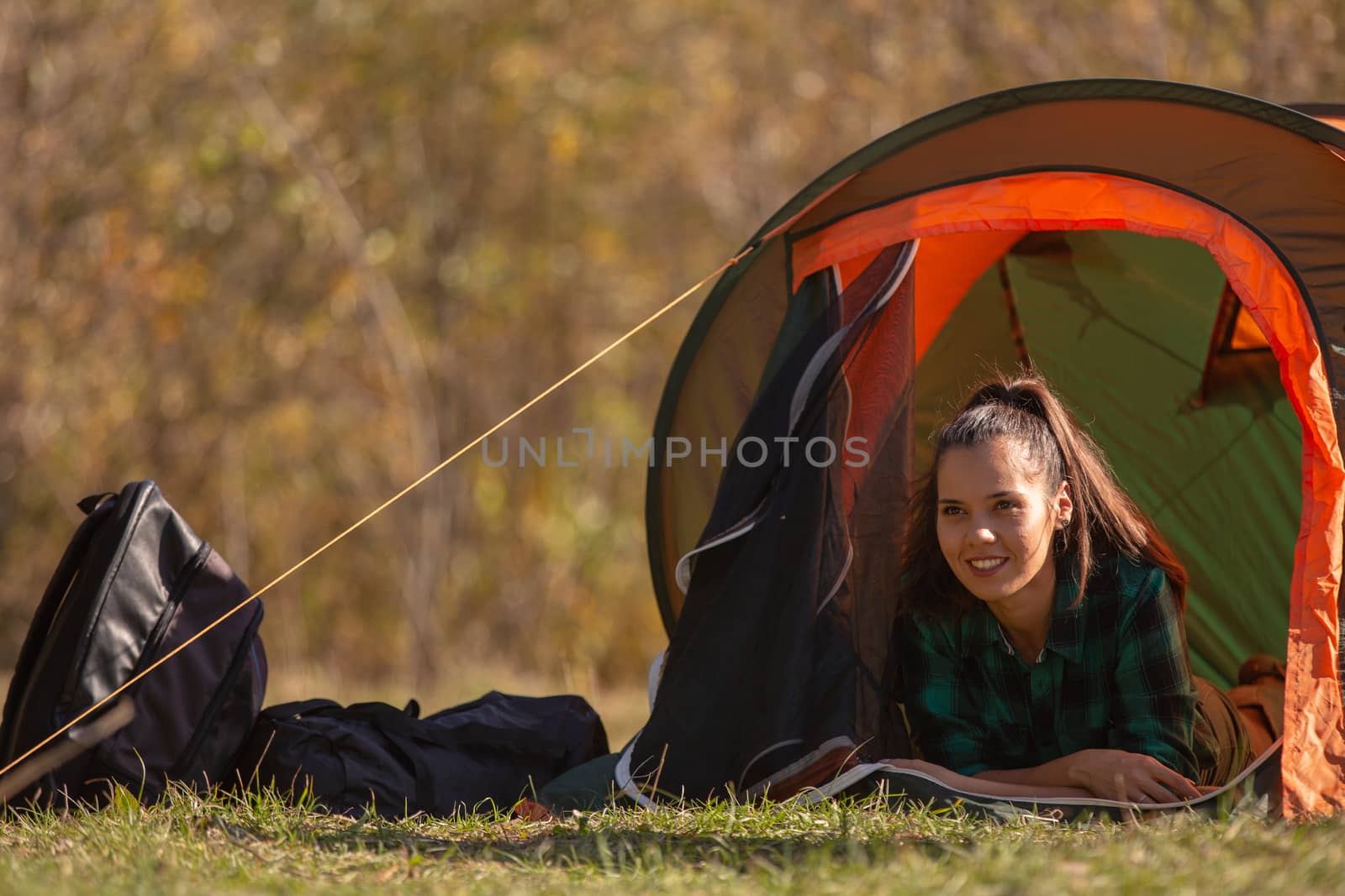 Smiling young woman standing in front of the tent. Forest background