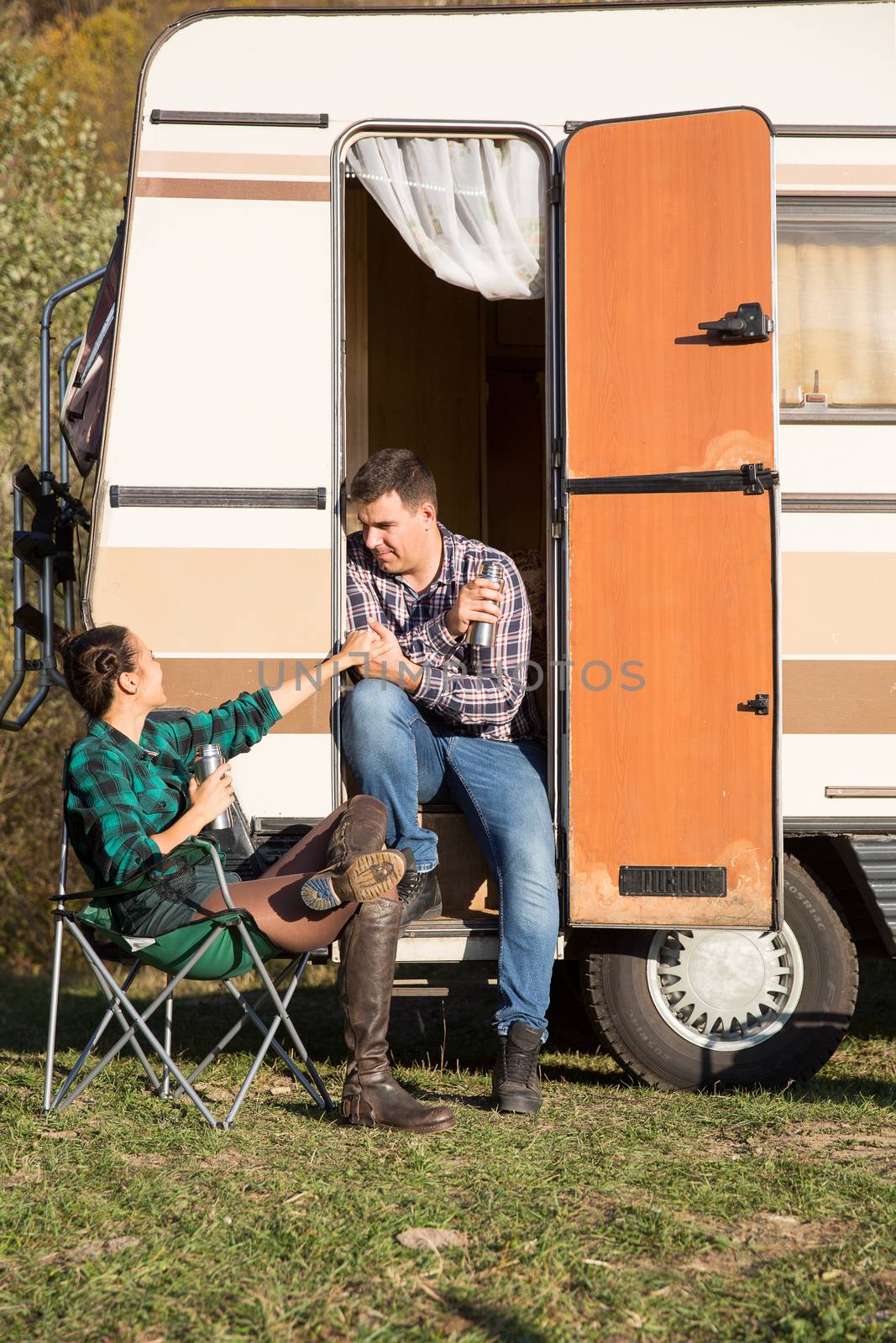 Woman sitting on camping chair and looking at her boyfriend sitting on the stairs of their retro camper van.