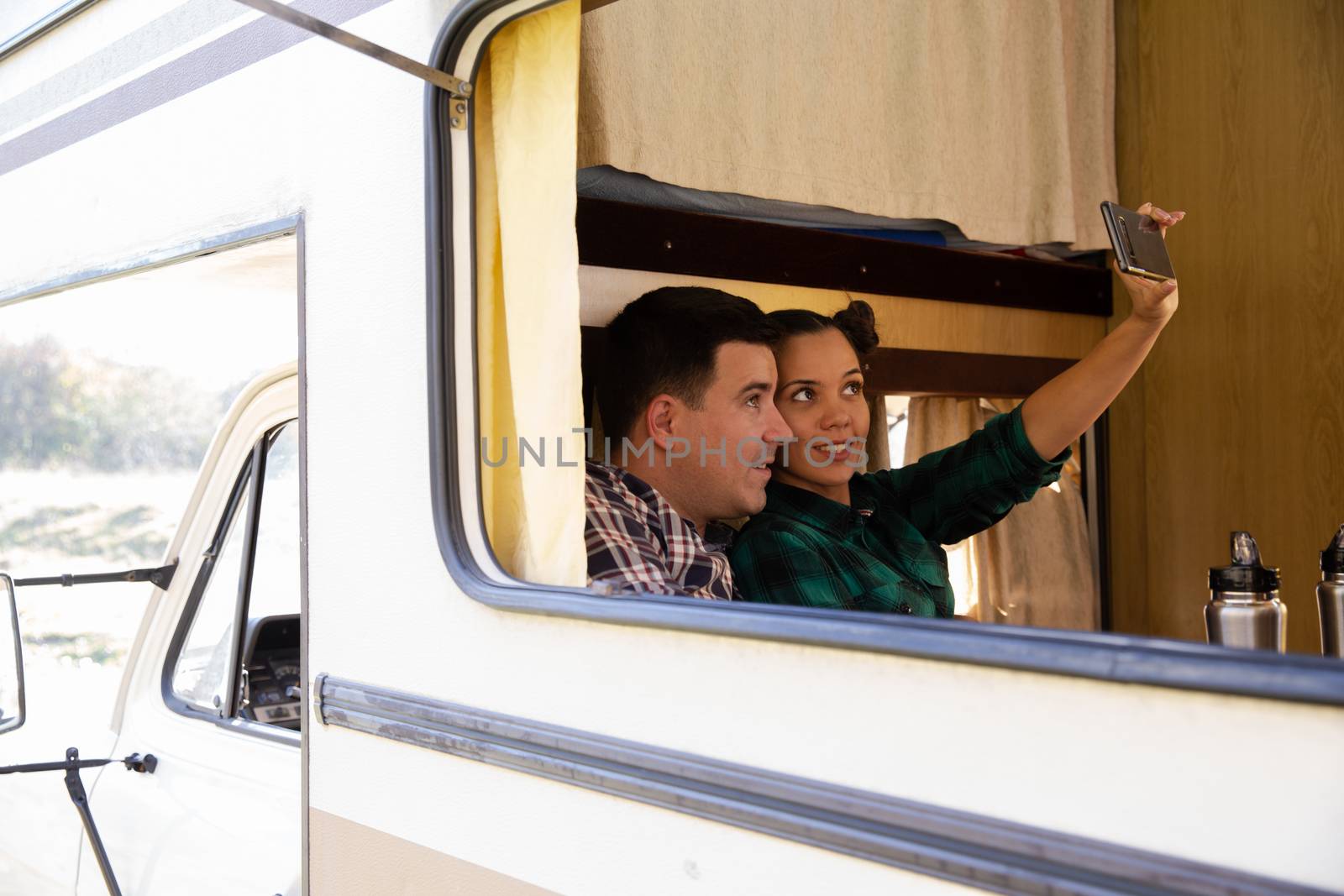Hipster couple sitting in their retro camper van and taking a selfie with phone.Romantic young couple.