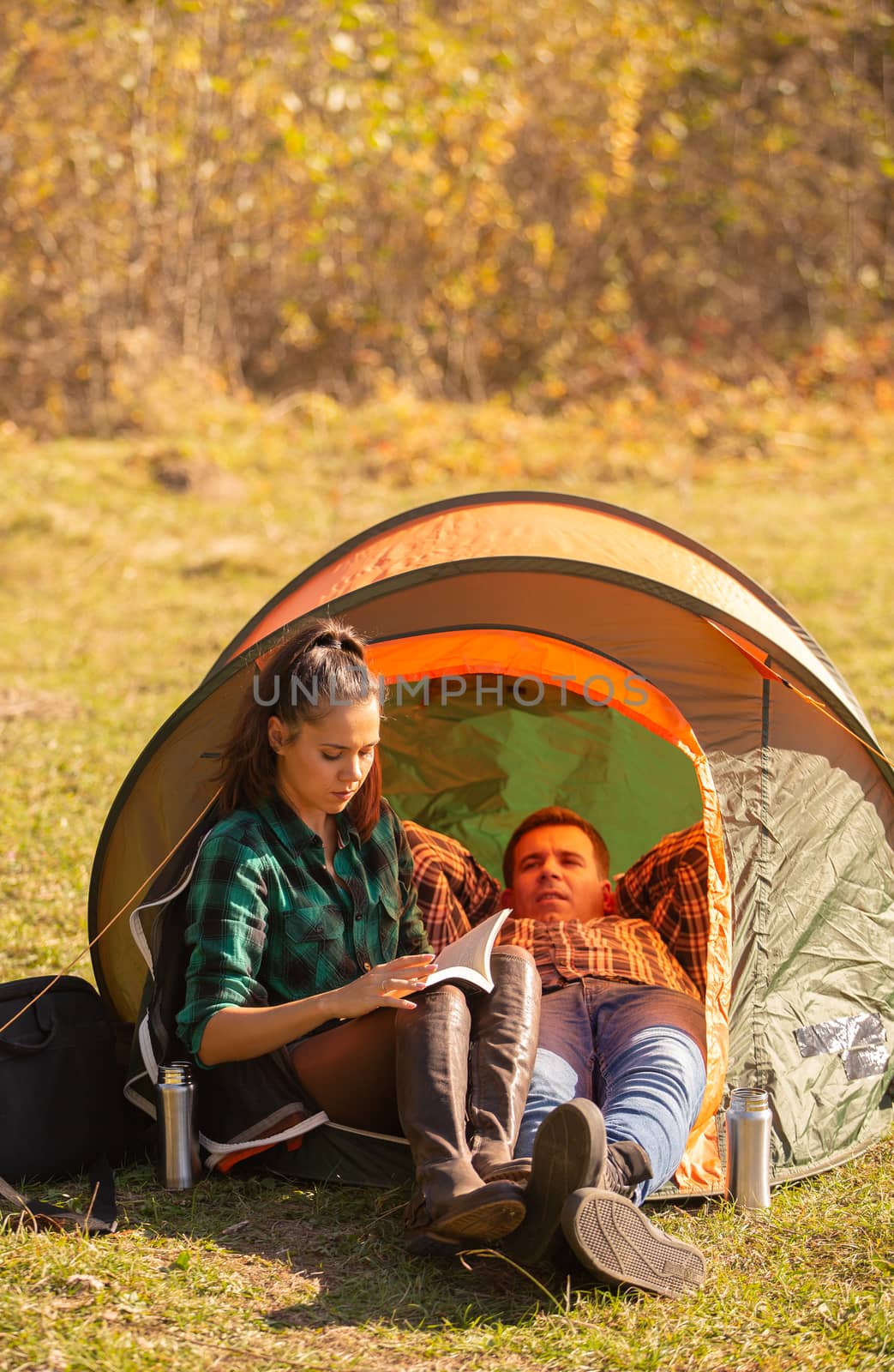 Young girl reading a book with her friend next to the tent. Relax vacation