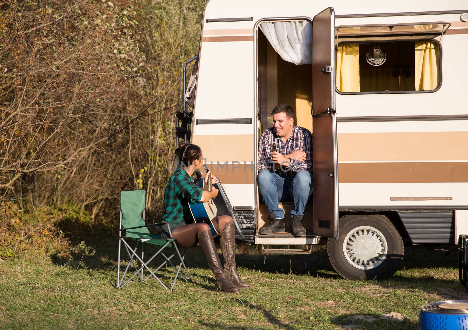 Woman playing on old guitar for his man in front of their retro camper van in the mountains.