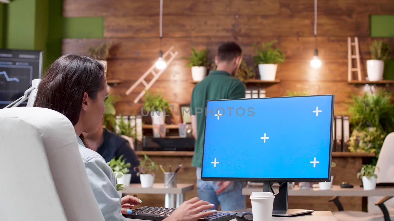 Wide shot of a woman working on a computer with isolated mock-up in a busy office