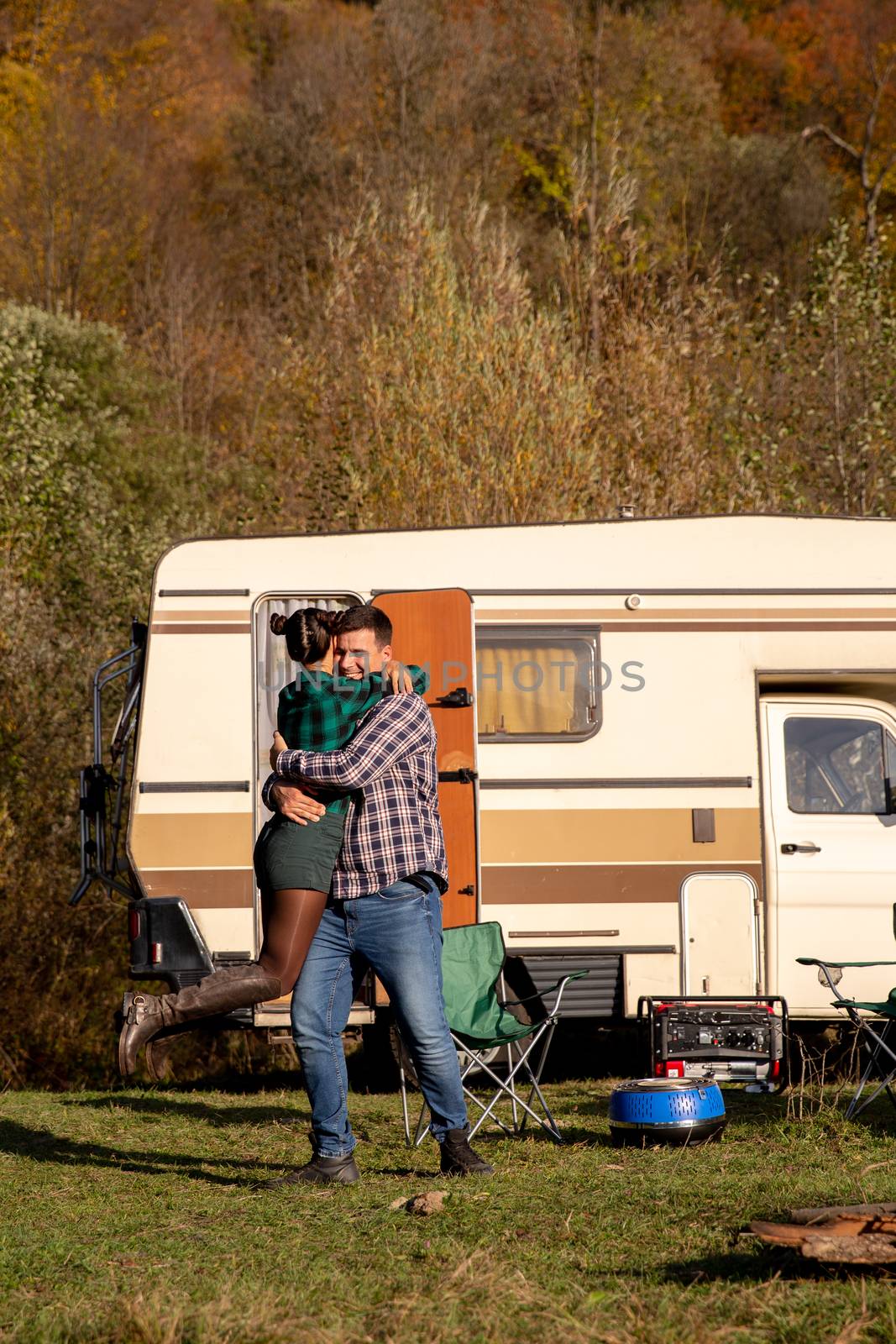 Beautiful young couple embracing themselves in a campsite with their retro camper van in the backgrounnd.