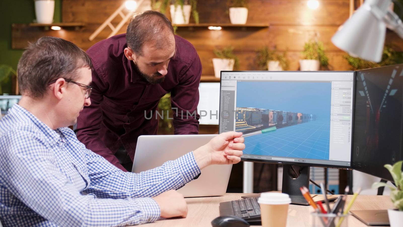 Graphic designer in game industry sitting at his office showing his assistant new gaming graphics.