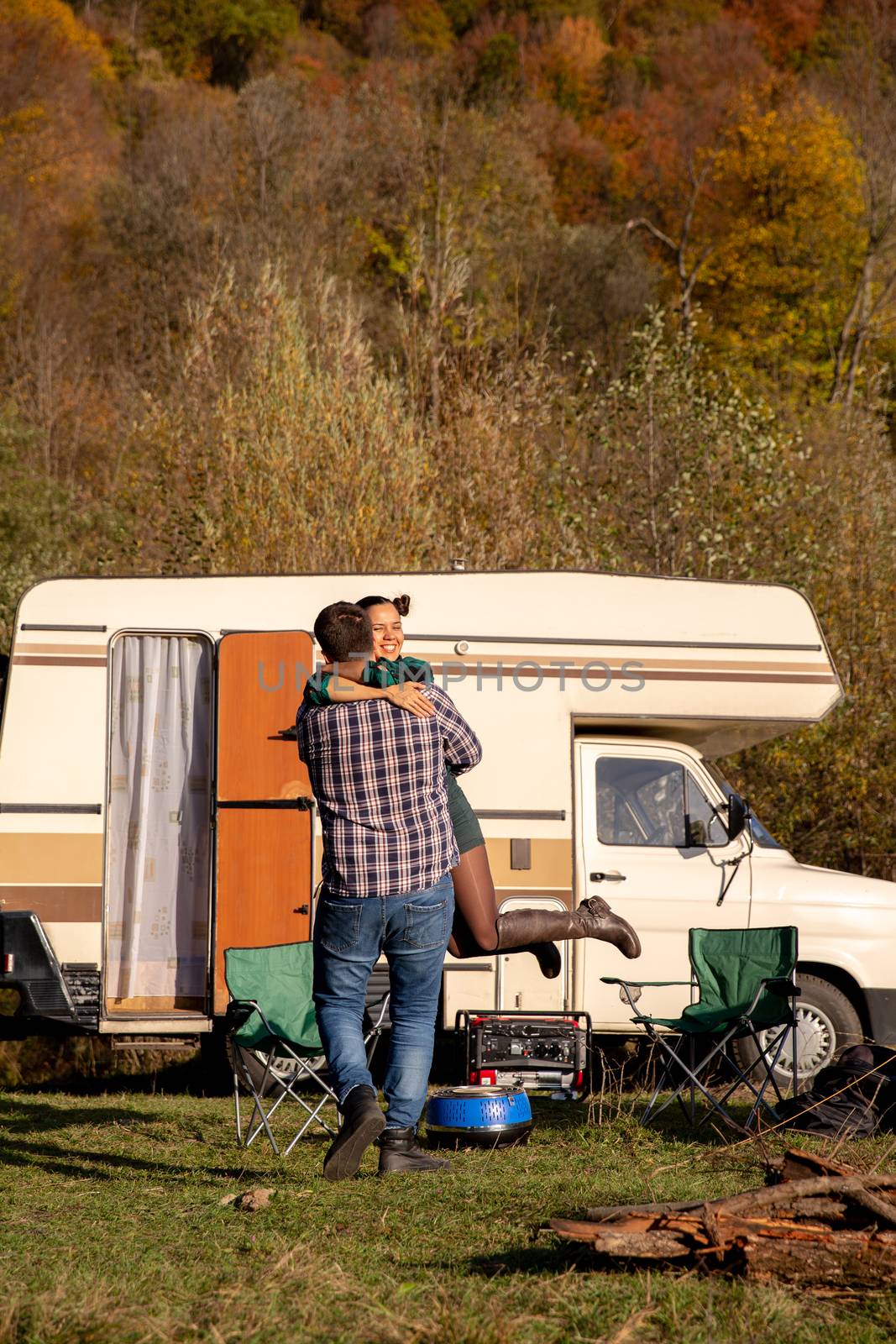 Playful boyfriend spinning her girlfriend in the air in front of their retro camper van.