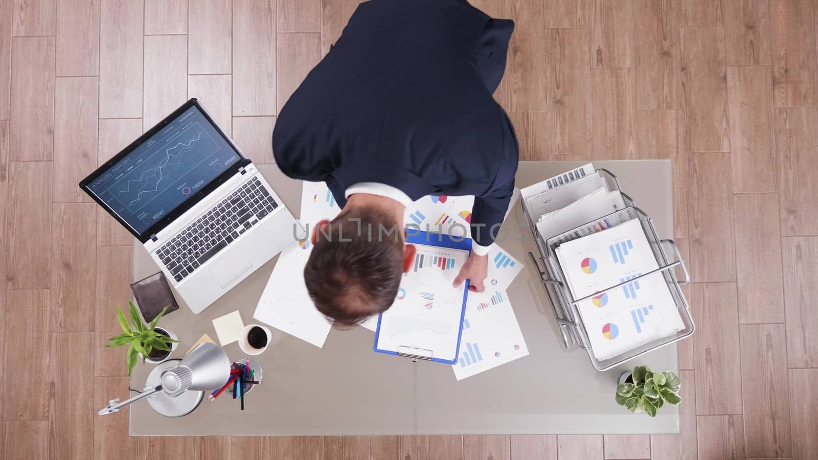 Top view of businessman in suit taking a sip of coffee and analysing documents in his office.