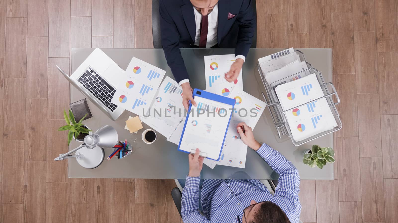 Top view of businessman in suit signing a contract after analysing agreement charts in a business meeting.