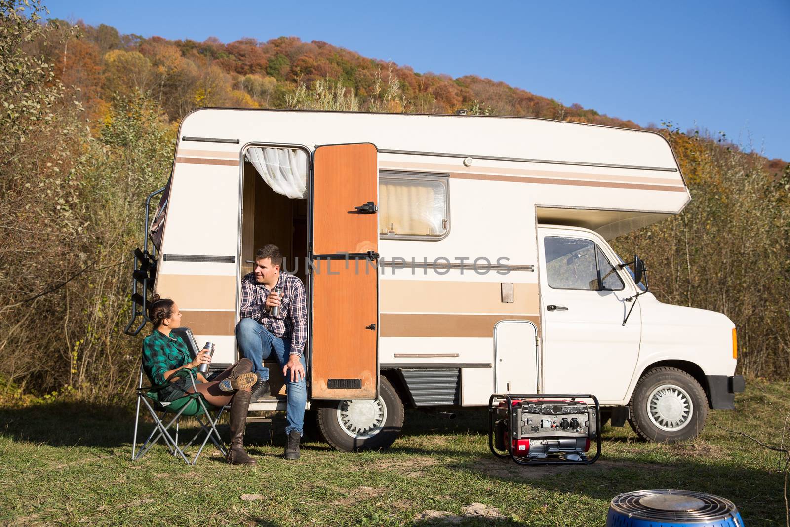 Man sitting on the stairs of his retro camper van in the mountains and talking with his girlfriend.