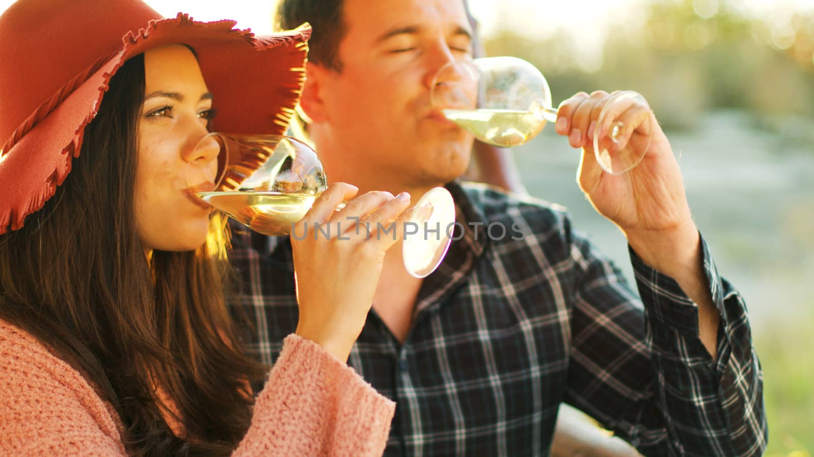 Close up shot of couple in sun flares having a tender moment with some glasses of white wine in hands.