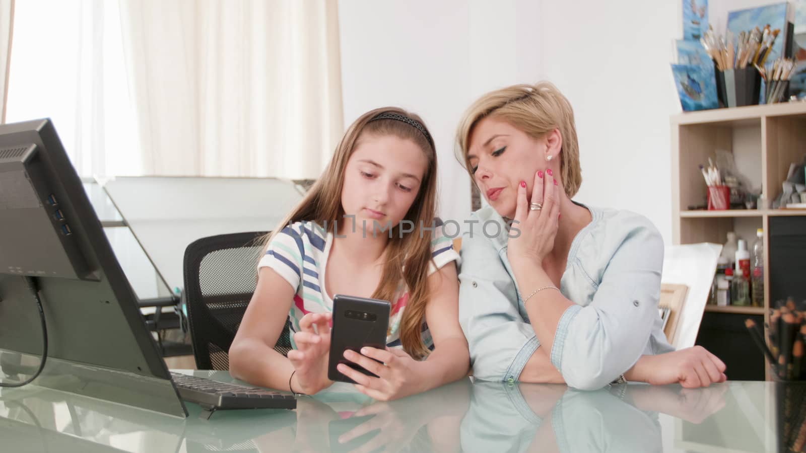 Young teenage girl showing something to her mother on a smartphone. Mom and teenage daughter looking at a smartphone screen.