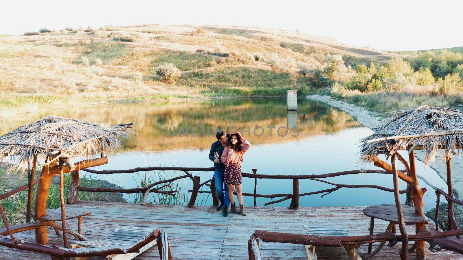 Flying over a couple tasting wine on pontoon near a lake in rural area, drone aerial shot