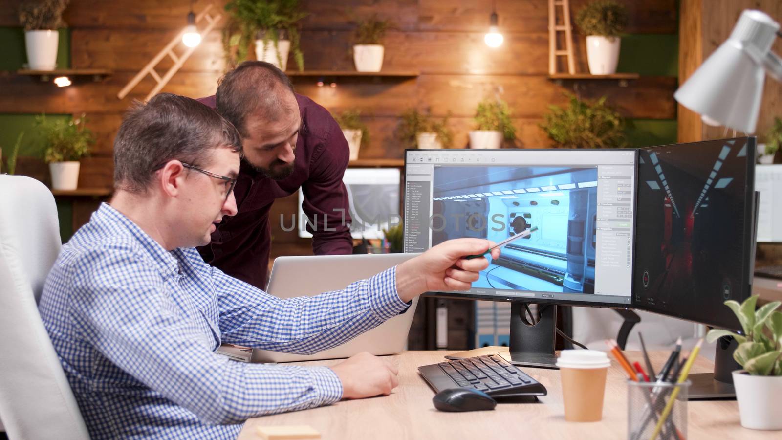 Graphic designer in game industry sitting at his office showing his assistant new gaming graphics.