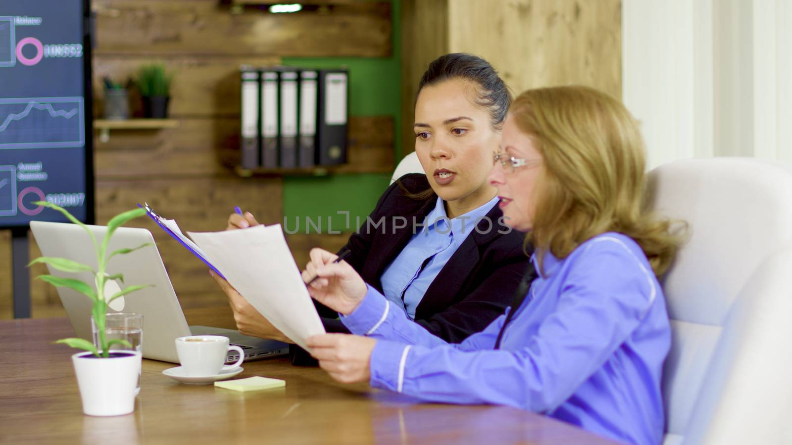 Two business women in the conference room looking at firm statistics report.