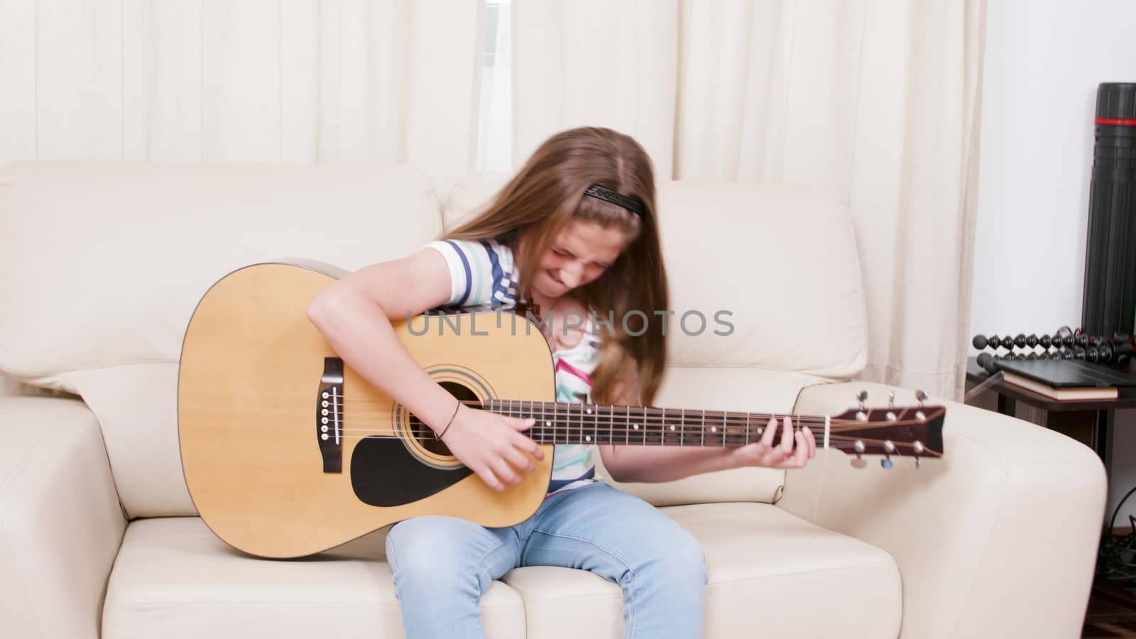 Teenage girl plays on an acoustic guitar sitting on a sofa. Teen playing on a musical instrument.