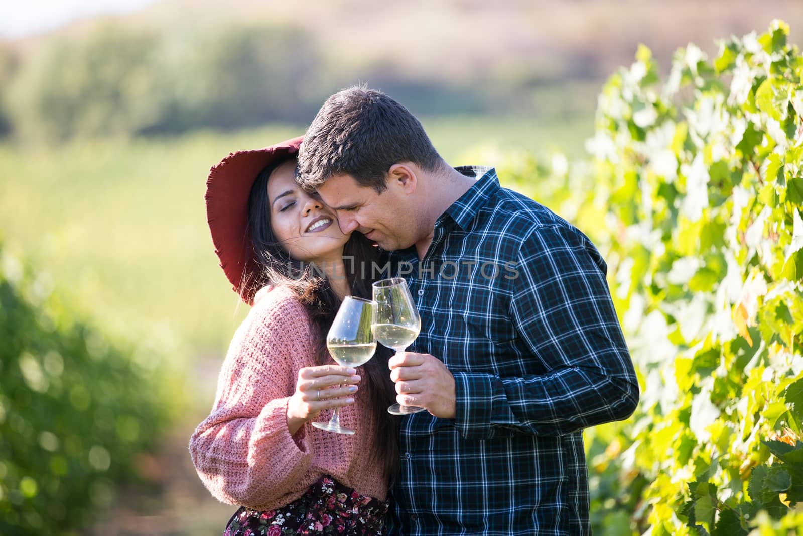 A young couple in love in the vineyards holding glasses of wine.