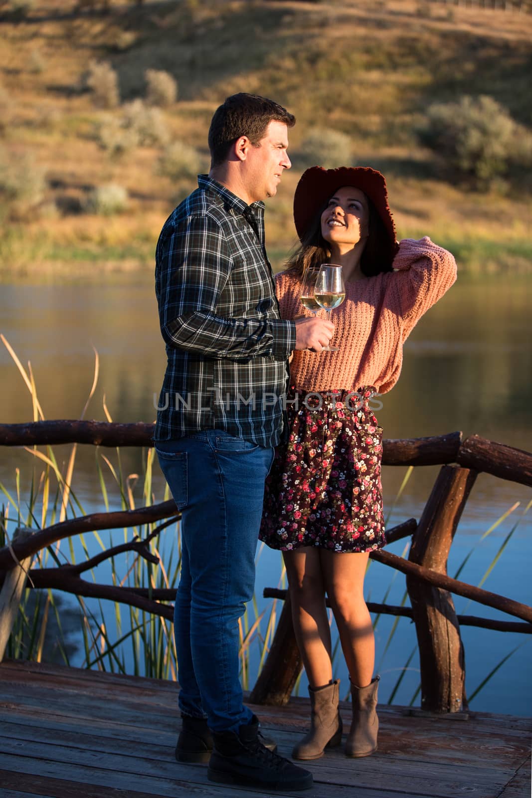 Young woman looking up to her husband on a wooden pontoon with lake behind the in the middle of a vineyard.