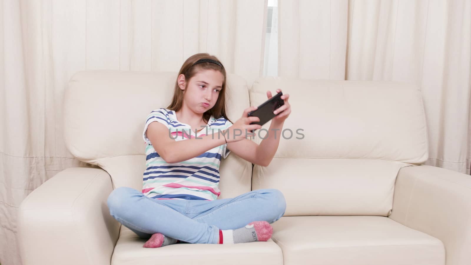 Teen girl on a sofa playing a game on a smartphone. Girl gaming on a smartphone in living room.