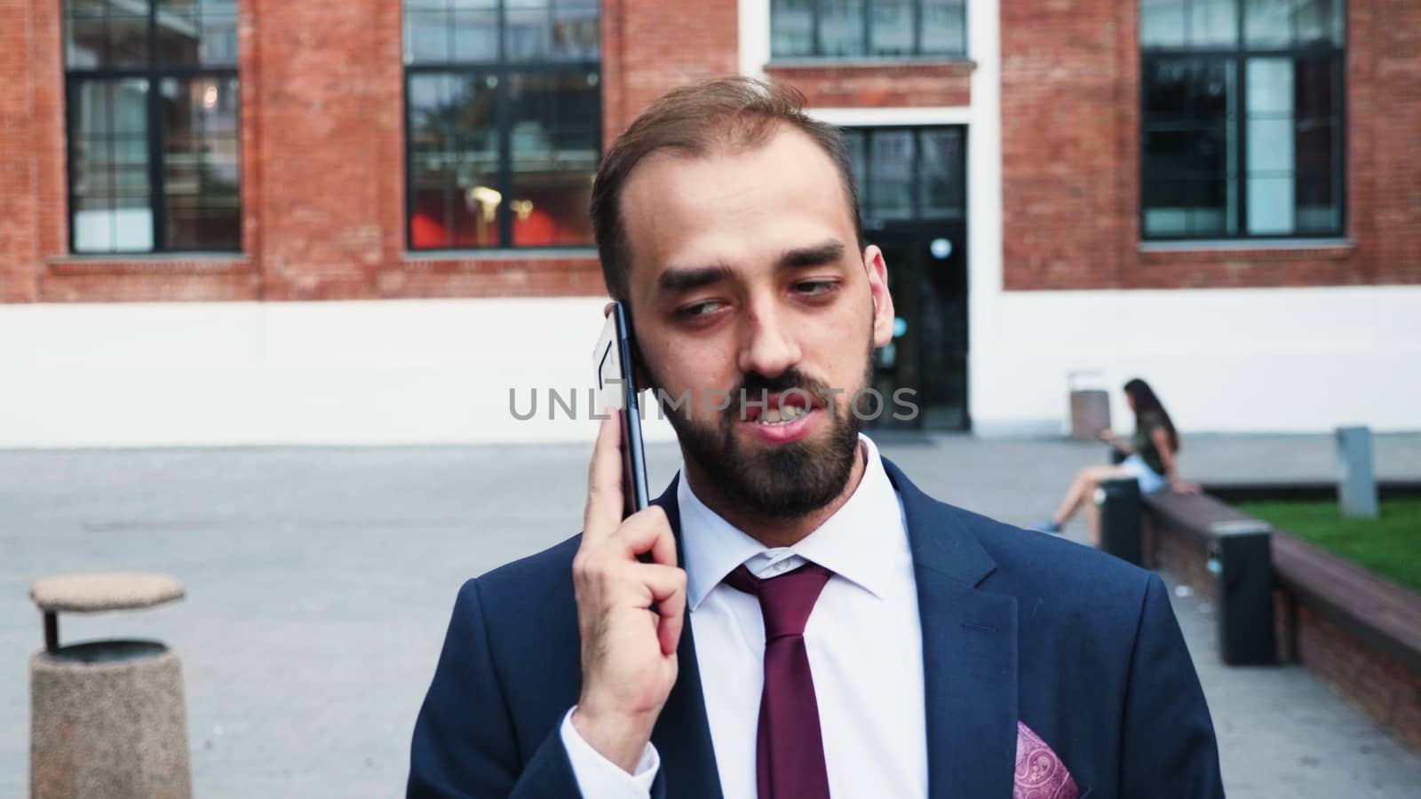 Businessman in suit walking and talking on the phone in front of the business district, slow motion outdoor shot