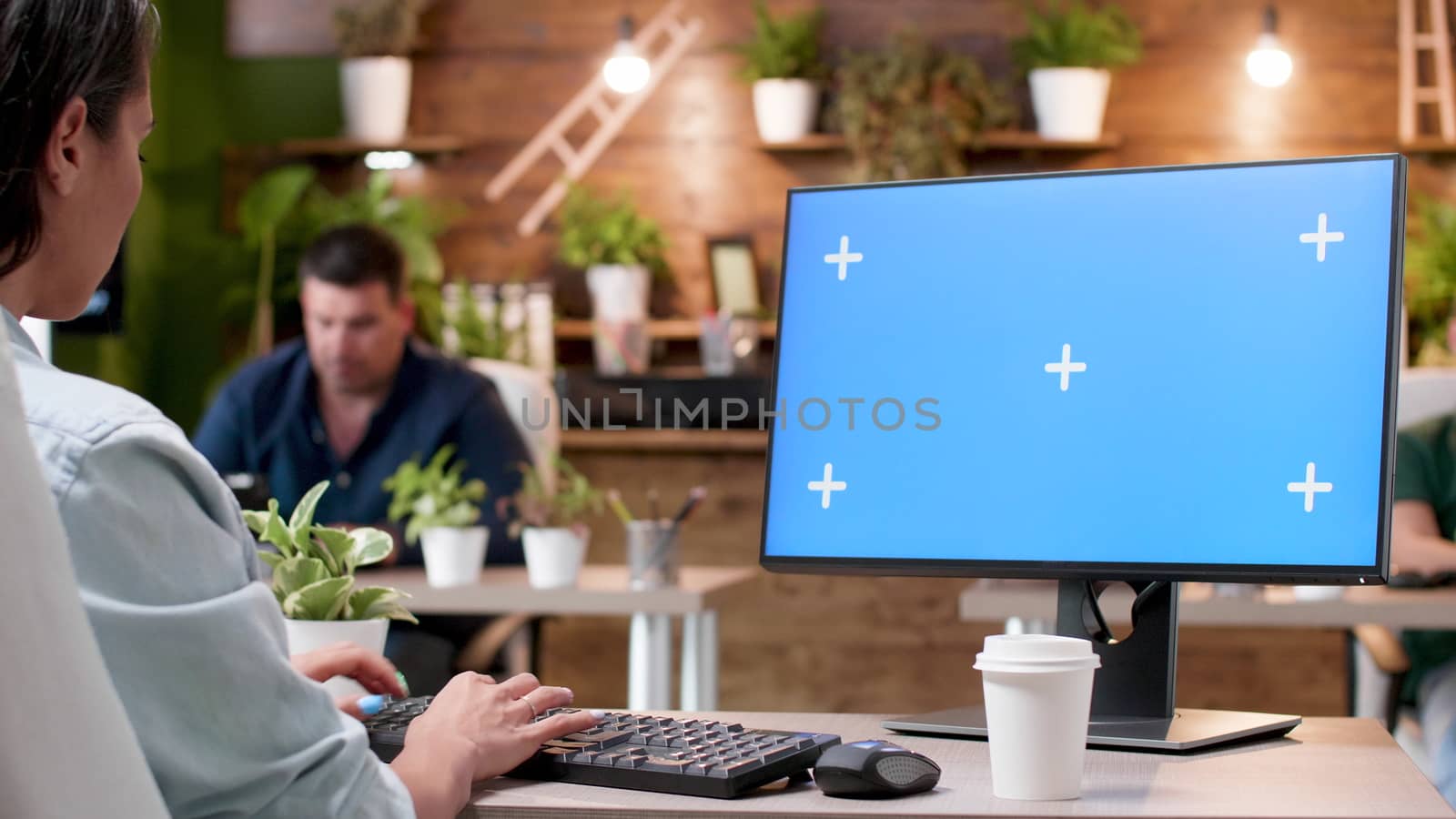 Woman typing on a computer with a blue screen mock-up in modern and cozy office