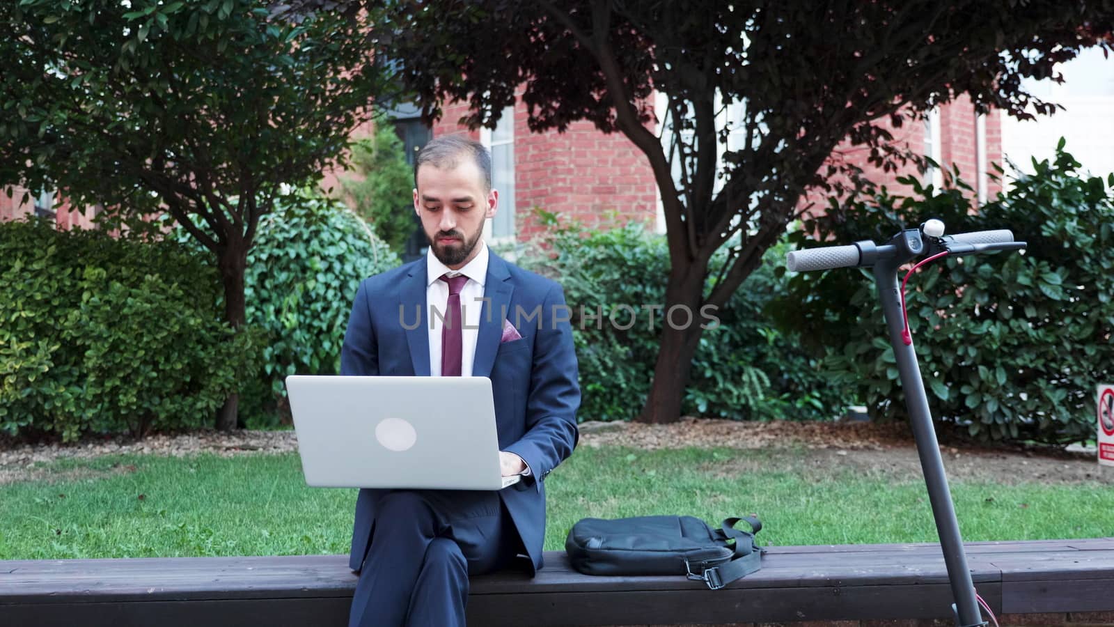 Manager working on the go on the laptop. He sitts outdoor and types on the computer. Slow motion shot