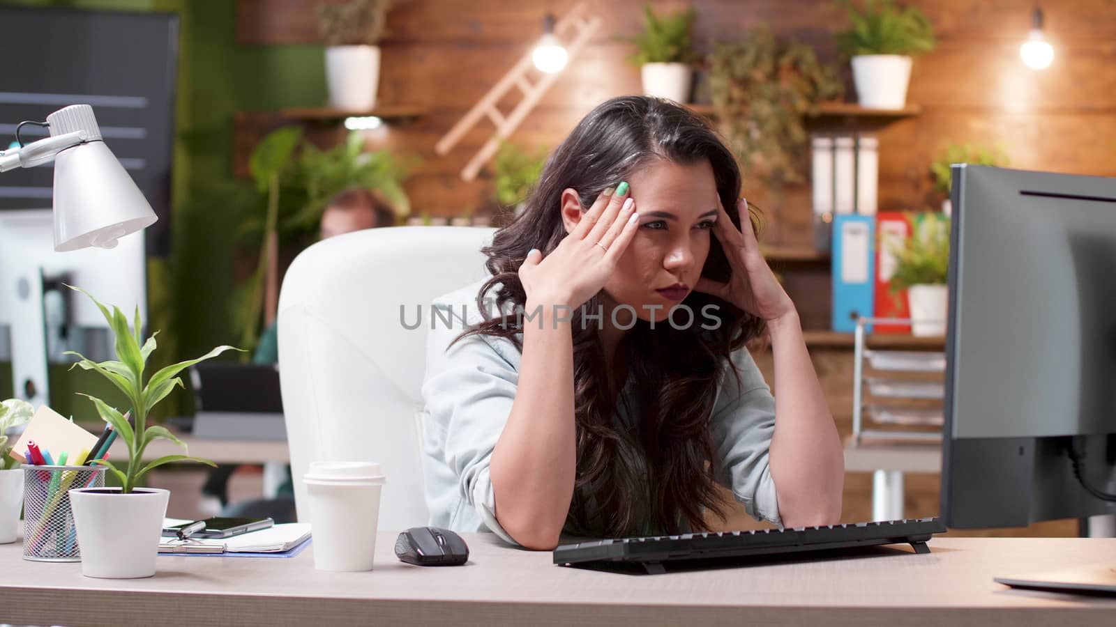 Stressed woman having a headache while working in the office. Exhausted and overworked girl. Busy team in the background.