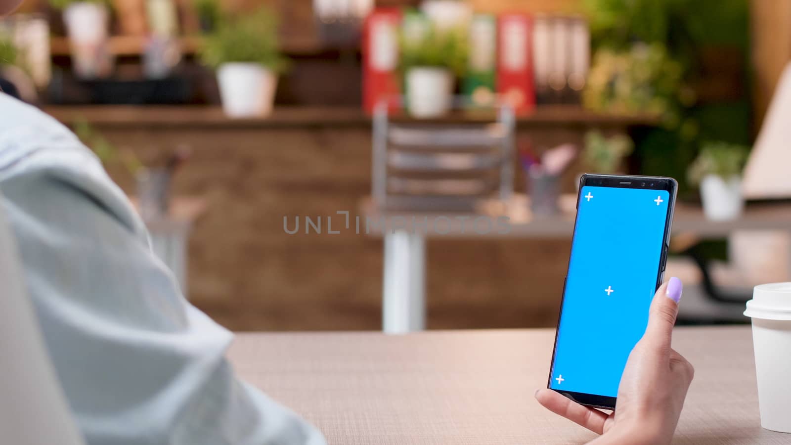 Woman hands holding a smartphone with an isolated mock-up screen in a busy office