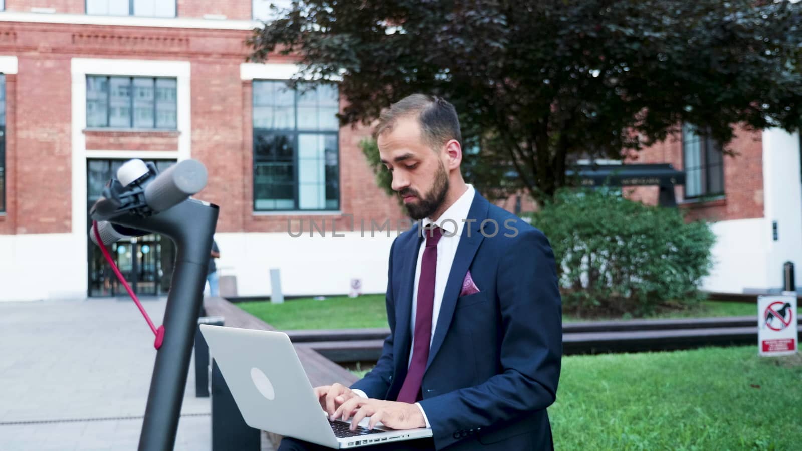 Confident businessman outdoor working on the computer, zoom in slow motion shot. He is in modern business district