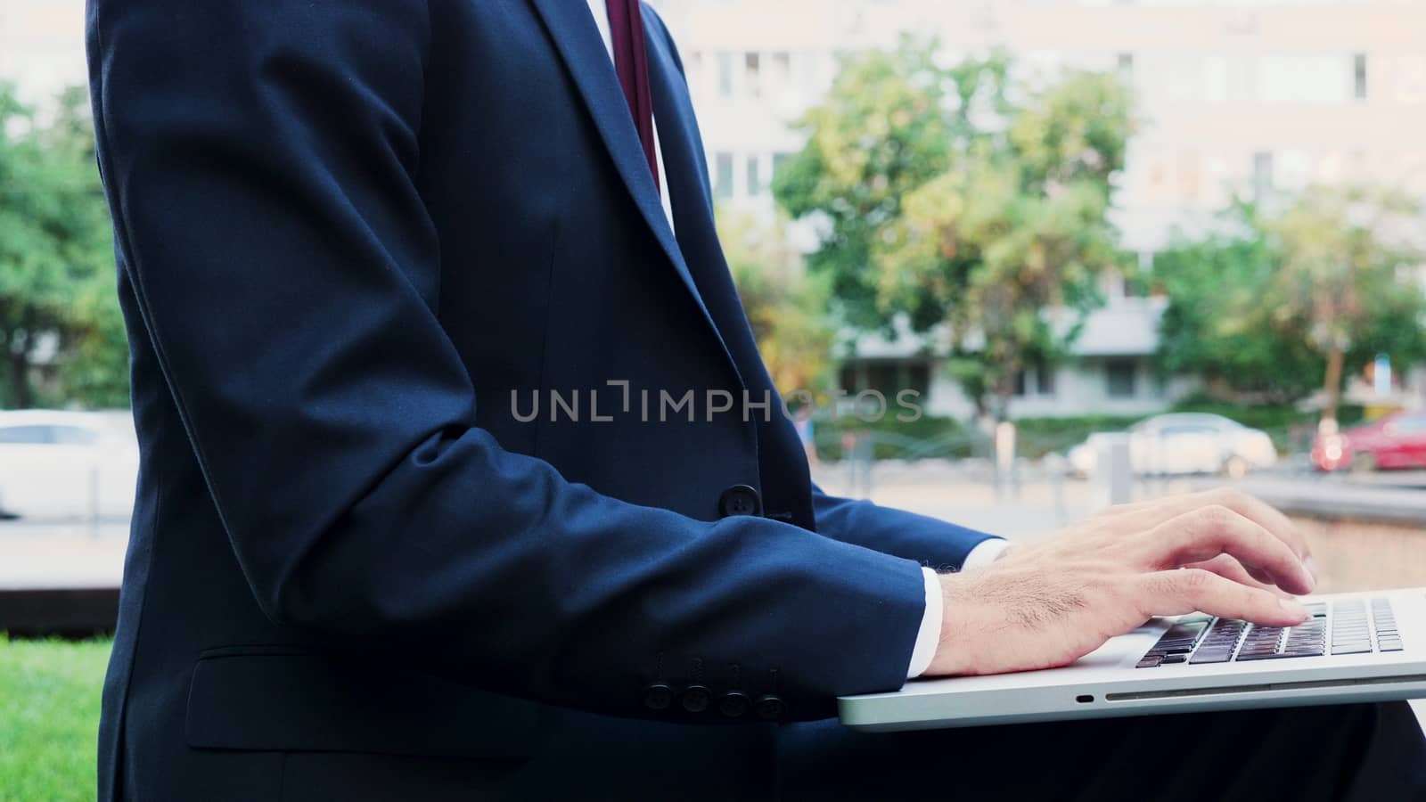 Businessman hands typing on laptop keyboard outdoor in the city, close up
