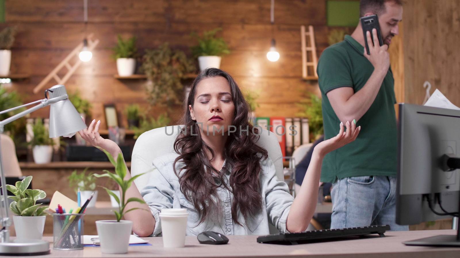 Woman meditates while her colleagues are throwing papers in the air in a very stressed work environment. Slow motion shot and conceptual footage