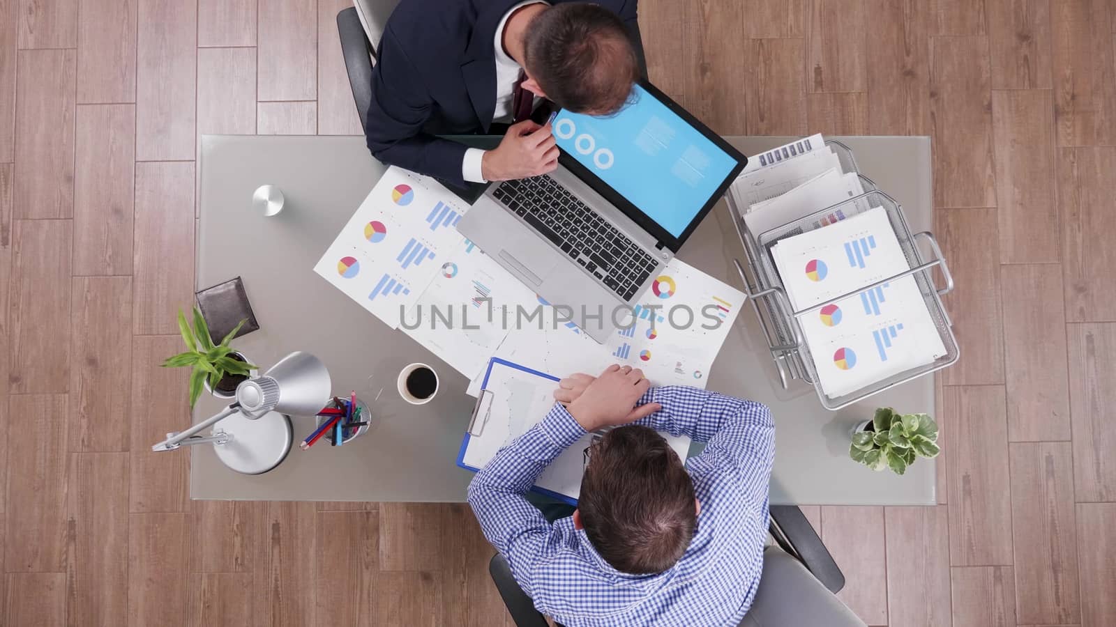 Top view of businessman in suit explaining charts from his laptop to new employee.