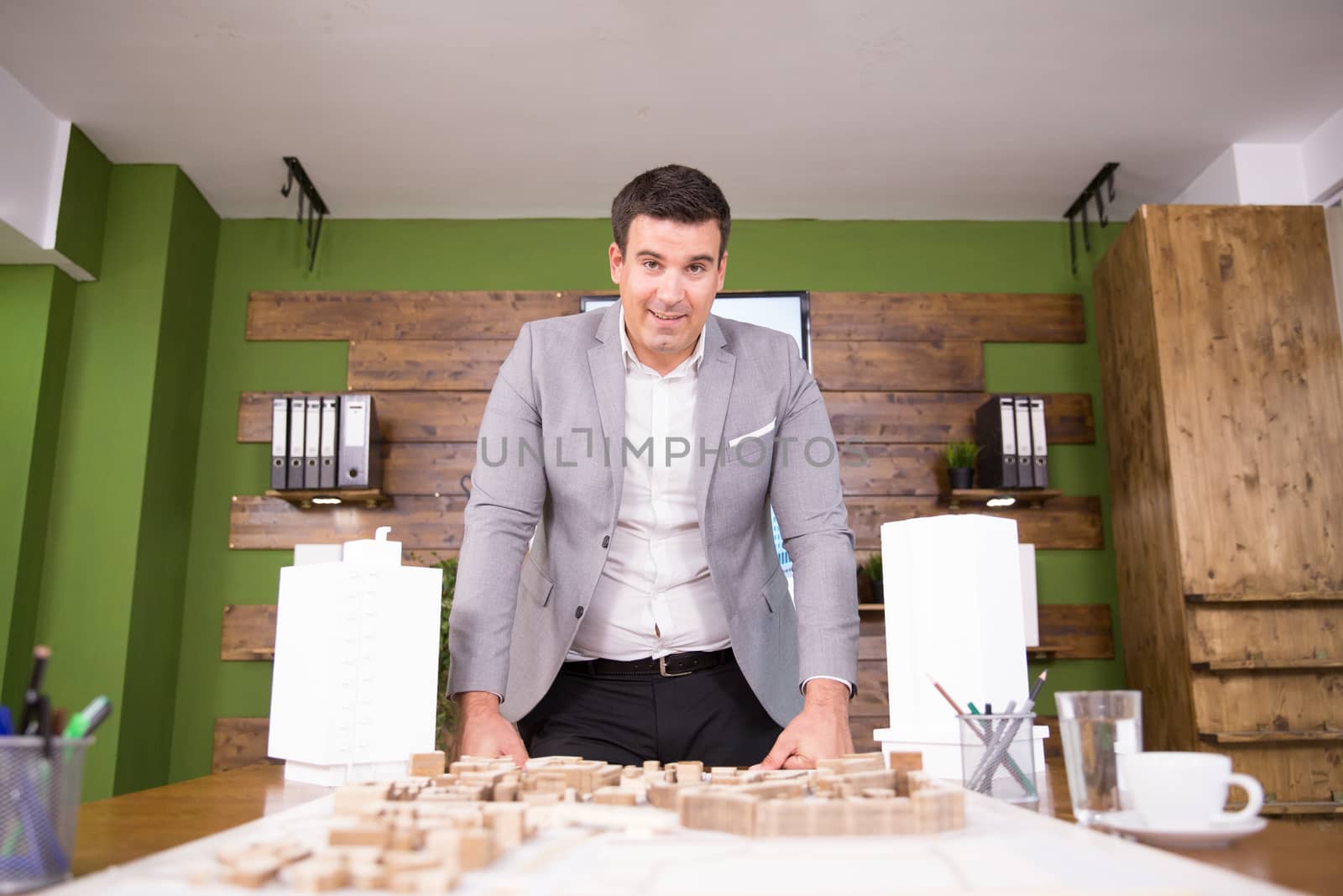 Young architect leaning over real estate project in a conference room. Mini town.