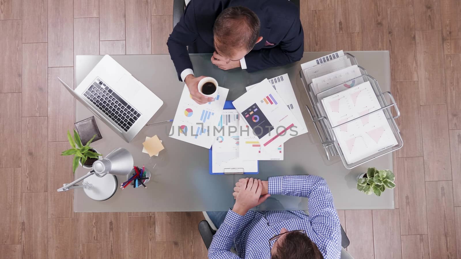 Top view of businessman in suit drinking coffee during a business meeting with a man in his office.