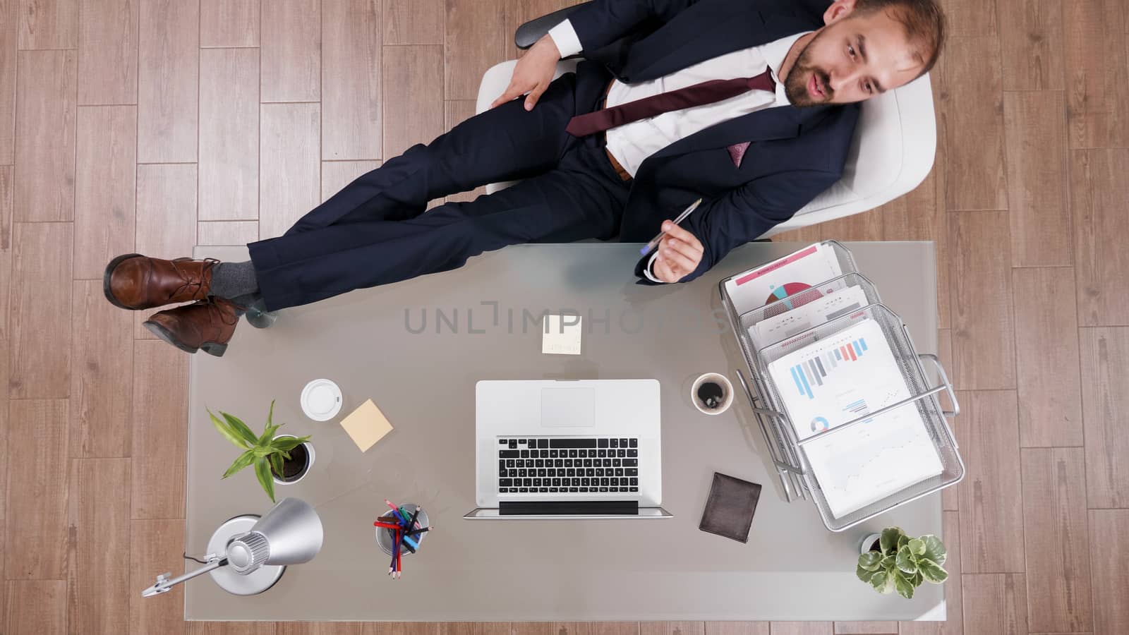Top view of successful businessman in suit with his feet on the desk and diagrams on it.