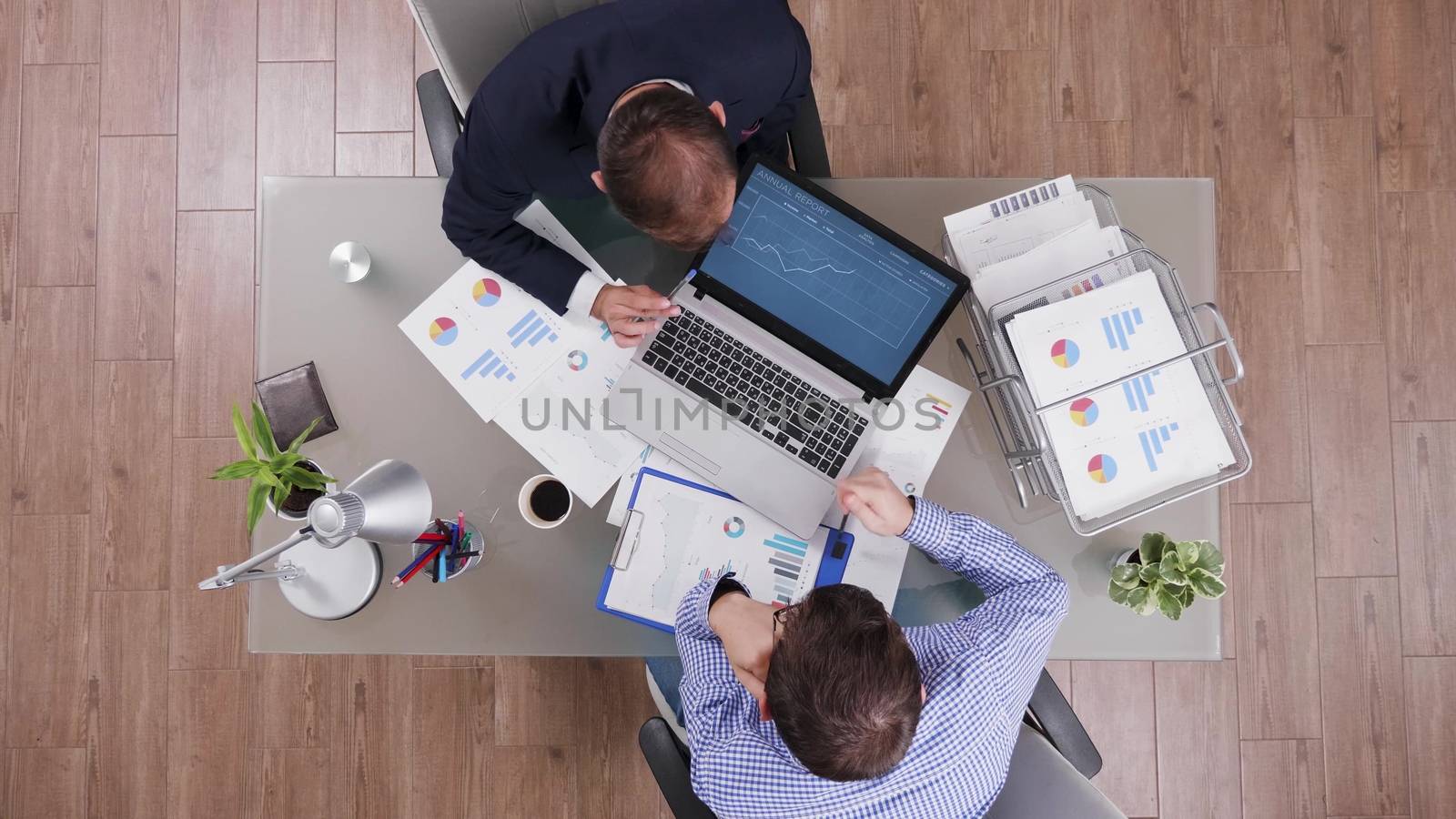 Top view of businessman in suit having a breefing and examining charts from laptop with his consultant.