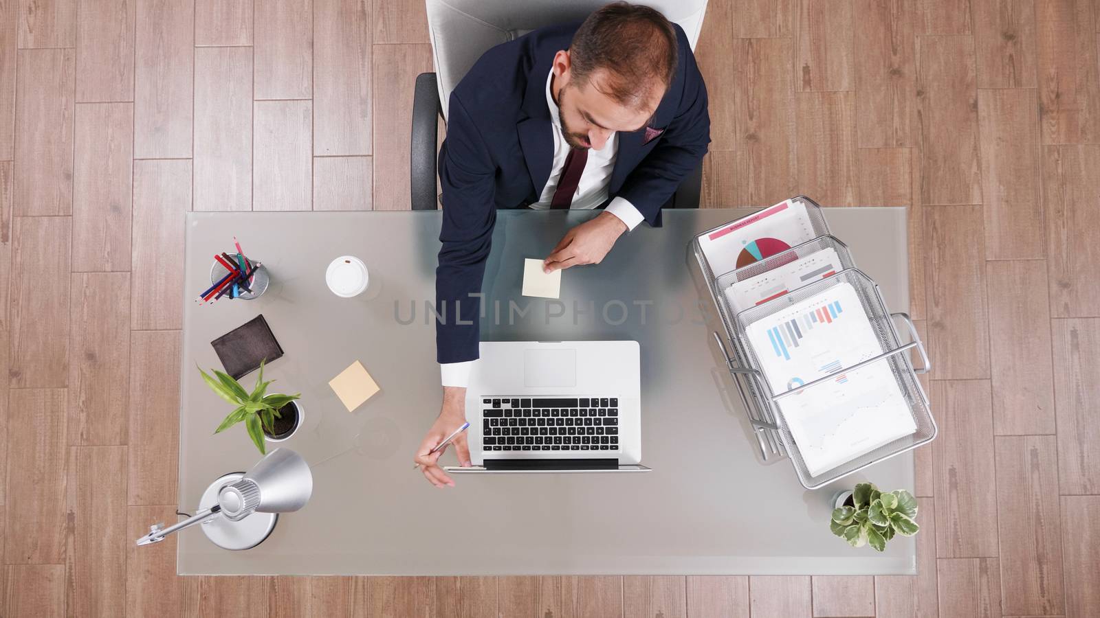 Top view of businessman in suit talking on the phone and taking notes sitting at his office.